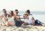 Grupa osób siedząca na plaży wokół ciemnoszarego barku z podniesionym blatem, wypełnionego lodem i butelkami.