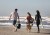 Widok z tyłu na trzy osoby z psem idące plażą, jedna z nich niesie ciemnoszary barek z uchwytem.